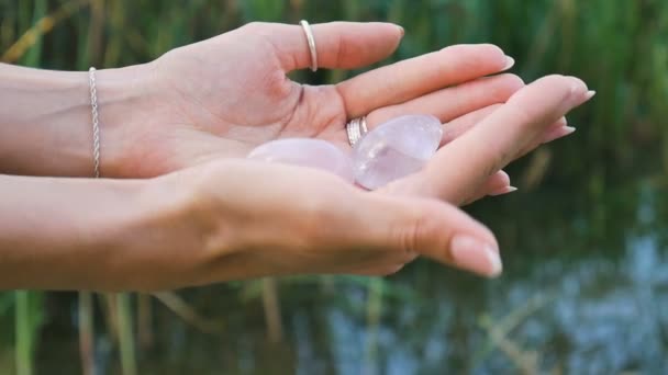 Vrouwelijke hand met een rozenkwarts en amethist kristallen yoni eieren op rivierachtergrond. Vrouwen gezondheid, eenheid met natuurbegrippen — Stockvideo