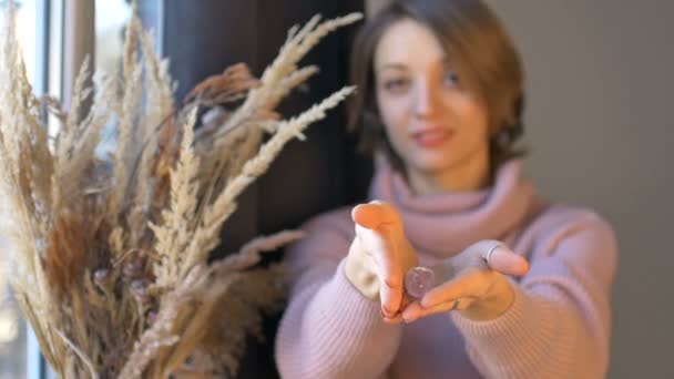 Woman is holding yoni egg made from transparent violet amethyst stone standing near the window with vase of spikelets. Female health concept, vumfit, imbuilding or meditation — Stock Video