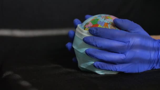 Aardebol met geografische namen in Oekraïense cyrillische letters erop gekleed in een chirurgisch masker in de handen van een arts in beschermende handschoenen. Coronavirusepidemie in de wereld — Stockvideo