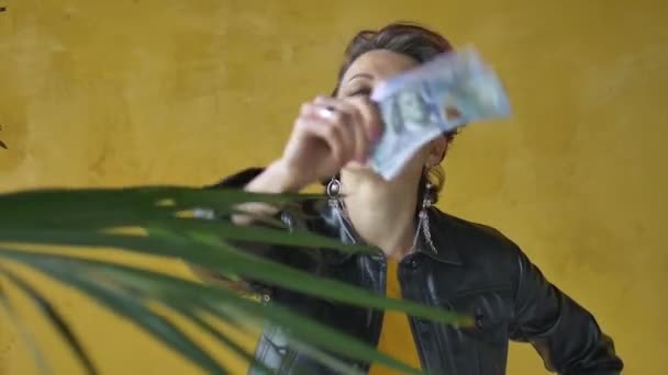 Glamorous aggressive lady in punk rock style party clothes with dark pink hair in black leather jacket and long earrings on yellow background with money dollars and hryvnias in hands — Stock Video