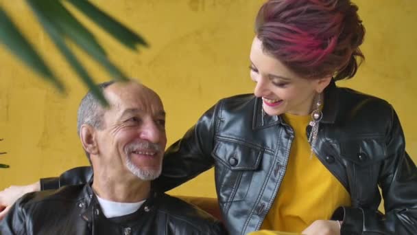Emotional family portrait of adult daughter and senior father in loft room with houseplants. Laughing man and girl in black leather jackets in punk style on yellow wall background — Stock Video