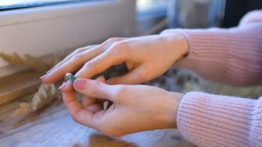 Doğal manikürlü kadın elleri, üzerinde çiviler olan tahta pencere pervazında turuncu ve yeşil değerli taşlardan yapılmış yüzükler gösteriyor.