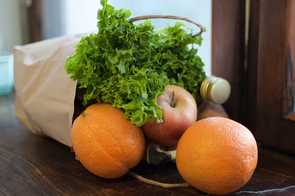 Produktset, grüner Salat und Früchte liegen in Bastelpapierverpackung auf der hölzernen Fensterbank. Lieferung von Lebensmitteln, richtiges Ernährungskonzept — Stockfoto