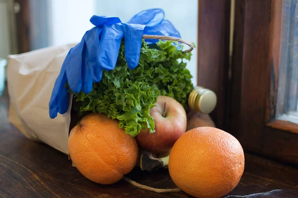 Produkt auf der hölzernen Fensterbank. Grüner Salat, Früchte liegen neben blauen Schutzhandschuhen. Essensausgabe während einer Coronavirus-Pandemie und Isolation. — Stockfoto