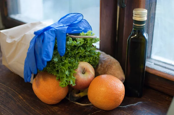 Produkt auf der hölzernen Fensterbank. Grüner Salat, Früchte und eine Flasche mit Öl liegen neben blauen Schutzhandschuhen. Essensausgabe während einer Coronavirus-Pandemie und Isolation. — Stockfoto