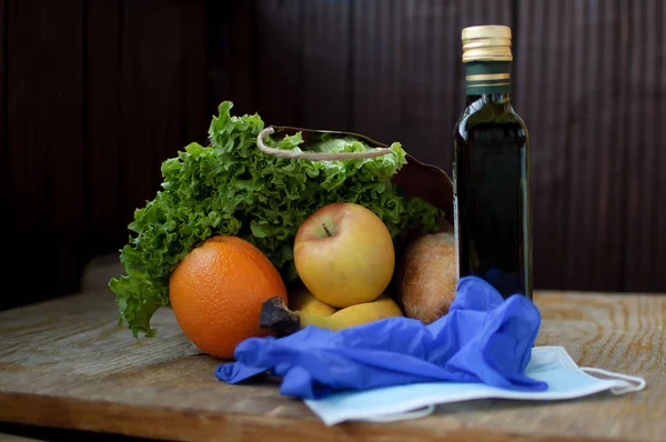 Produkt auf der hölzernen Fensterbank. Grüne Salatblätter und Früchte liegen neben Operationsmaske und blauen Schutzhandschuhen. Essensausgabe während einer Coronavirus-Pandemie und Isolation. — Stockfoto