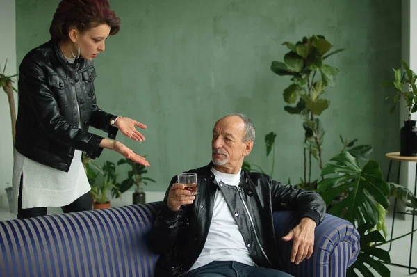 Эмоциональная взрослая дочь разговаривает со своим пьяным старшим отцом с бокалом виски или бренди в руке. Алкогольная зависимость, алкоголизм в семейных понятиях — стоковое фото