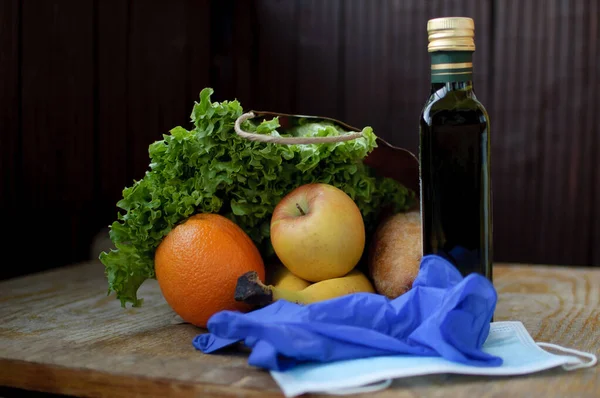 Product set on the wooden windowsill. Green leaves of the salad and fruits lying near surgical mask and blue protective gloves. Delivery food during a Coronavirus pandemic and isolation.