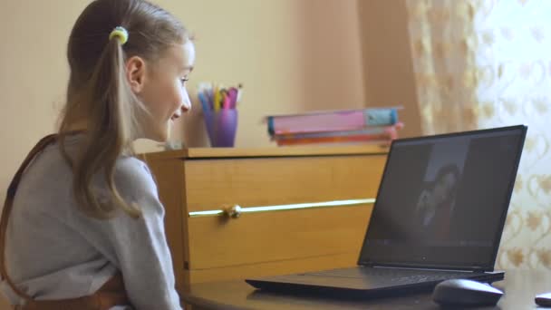 Back view of little girl with two ponytails sitting in front of the screen of her black laptop and studying at home because of the self-isolation due to Coronavirus Covid-19. Remote education — Stock Video