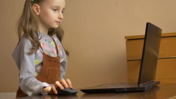 Schockiert überrascht, versucht das kleine Mädchen, ihre komplizierten Hausaufgaben mit einem schwarzen Laptop zu erledigen und hat keine Ahnung, wie sie während der Selbstisolation aufgrund der Pandemie des Coronavirus Covid-19 fertig werden soll. — Stockvideo