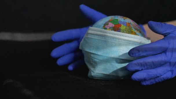 Jorden jordklotet med geografiska namn i ukrainska kyrilliska bokstäver på det klädd i en kirurgisk mask i händerna på en läkare i skyddshandskar. Coronavirusepidemi i världen — Stockvideo