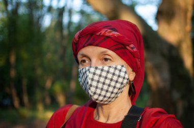 Parktaki güneşli bahar gününde, Coronavirus salgını nedeniyle el yapımı tekstil maskesi takan olgun bir kadın.