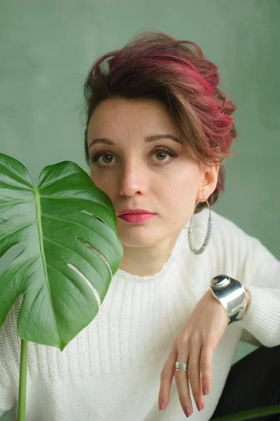 Retrato de uma jovem mulher bonita com pele lisa perfeita com uma grande folha tropical verde. Moda, beleza, maquiagem, cosméticos, saúde, ecologia, natureza, spa, bem-estar . — Fotografia de Stock