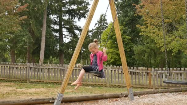 Bambina bionda scalza che si diverte su un'altalena all'aperto durante la giornata estiva di sole sul parco giochi in giardino, concetto di infanzia felice — Video Stock