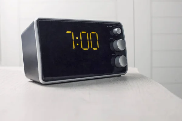 Digital alarm clock with yellow digits showing seven oclock — Stock Photo, Image