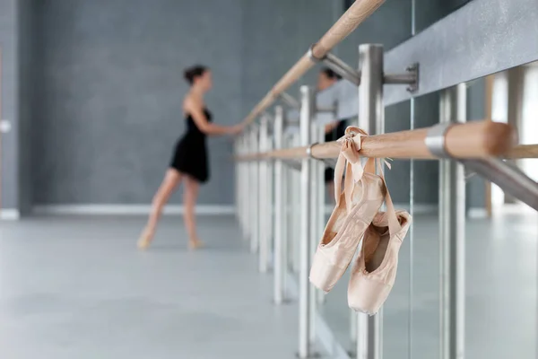 Pointe shoes hang on ballet barre. Ballerina has dance workout. Girl is doing exercises in front of mirror in ballet classic school.
