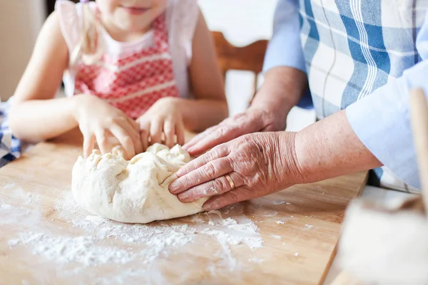 Family is preparing dough for baking in kitchen. Graceful hands of retired woman and kid are cooking
