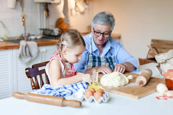 Grandmother is teaching child to cook pastries and food in cozy kitchen at home.