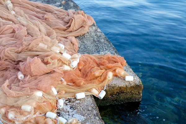 Fishing net on stone pier by sea. Fishermen tackle, ropes and fishnets piled on a wharf.