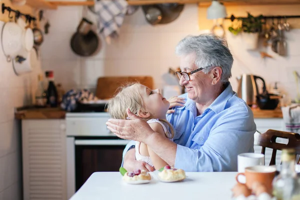 Happy grandmother is hugging child in cozy kitchen at home.