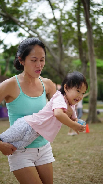 Азиатка, несущая малыша и участвующая в семейных играх на открытом воздухе — стоковое фото