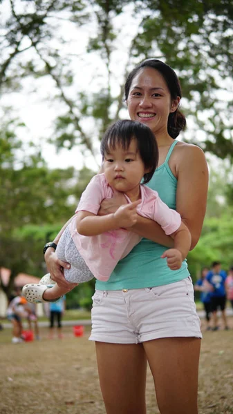 Mujer asiática llevando niño pequeño y participando en juegos familiares al aire libre —  Fotos de Stock