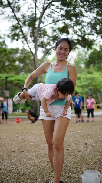Asian woman carrying toddler and participating in family games outdoor — Stock Photo, Image