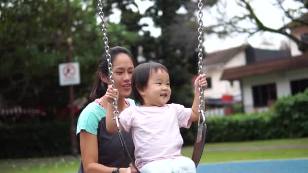 Slowmotion asiatiska kinesiska mor och dotter limning på en swing på lekplatsen — Stockvideo