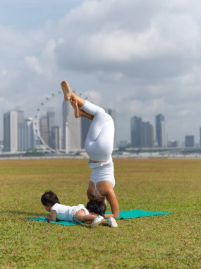 Asian chinese woman practising yoga outdoors with young baby girl clipart