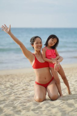 Asyalı Çinli kadın kızıyla kumsalda vakit geçiriyor.