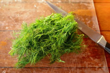 Dal taze yeşil dereotu su ile ahşap bir masaya bırakır. Doğal bir arka plan üzerinde büyük metal bıçak. Seçici odak.