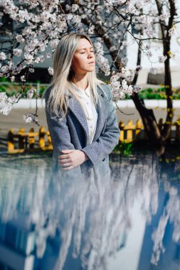 Dalgın genç sarışın kız bahar çiçekleri arasında duygusal portresi. Uzun saçlı genç bir kız bahar güneş ışınlarının gözlerinden kapalı.