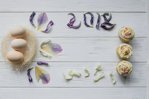 Великодня композиція з яйцями і сушеними фіолетовими пелюстками квітів. Надпис 2018 року, простір для тексту — стокове фото