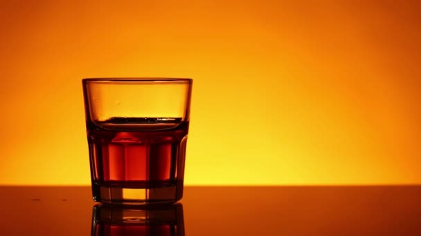 Pace di ghiaccio sta cadendo in un bicchiere di whisky, scotch o bourbon — Video Stock