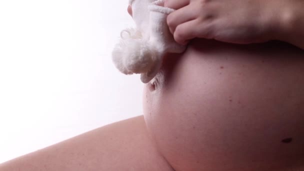 Una mujer embarazada se pone calcetines blancos en su vientre desnudo para recién nacidos — Vídeo de stock