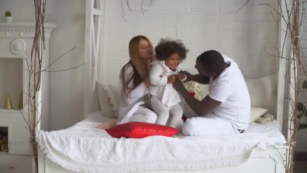 Joven familia multiétnica feliz de madre, padre e hija pequeña vestida de blanco en el fondo del árbol de Navidad y Año Nuevo en casa. Concepto de Navidad — Vídeo de stock