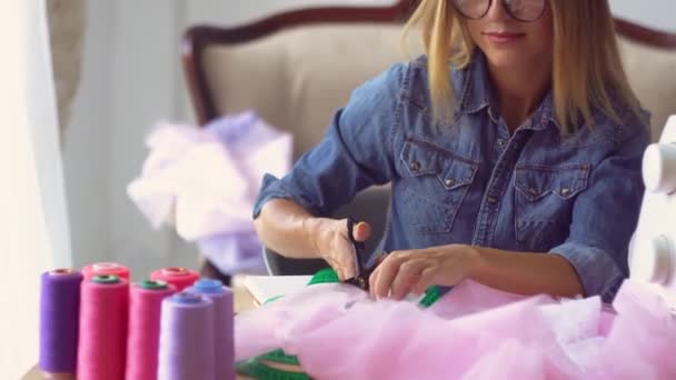 Швея блондинка в швейной мастерской работает с тканями за столом — стоковое видео