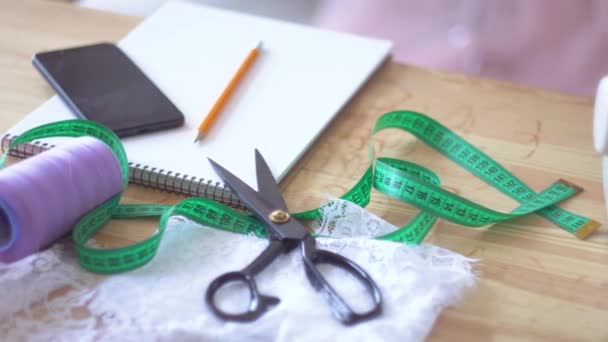 Outils à coudre sur la table : ciseaux, ruban à mesurer, bloc-notes, fils, tissu — Video