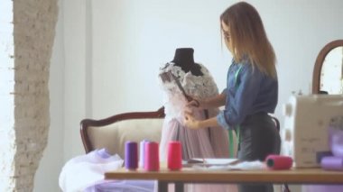 Dikiş atölyesindeki güzel terzi sarışın kuklanın yanında kumaşla çalışıyor. Kadın kıyafetleri modelleme süreci.
