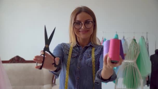 Krásná švadlena blondýny v šicím studiu drží šicí nůžky a přadénka nitě — Stock video