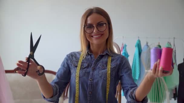 Hermosa costurera rubia en el estudio de costura sostiene tijeras de costura y madejas de hilo — Vídeo de stock