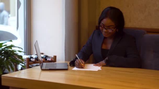 Femme d'affaires afro-américaine travaillant avec un ordinateur portable et des papiers. Femme occupée à payer des factures bancaires en ligne gérer les finances vérifier le budget faire de la paperasserie à l'aide d'un ordinateur assis au bureau — Video