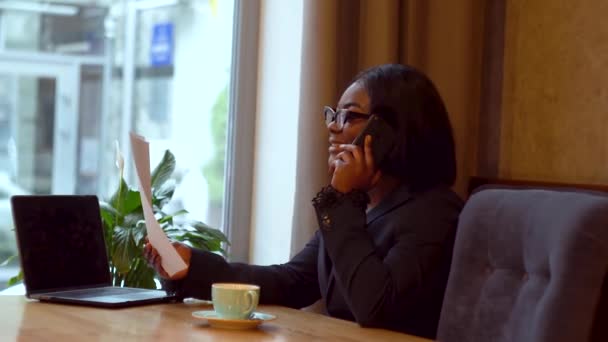 Femme d'affaires afro-américaine travaillant avec un ordinateur portable et des papiers. Fille parlant au téléphone avec un partenaire d'affaires — Video