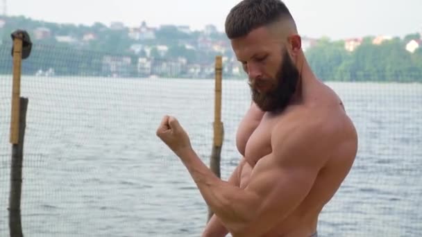 Bodybuilder demonstrates muscles. Young bearded athletic bodybuilder plays sports outdoors — Stock Video