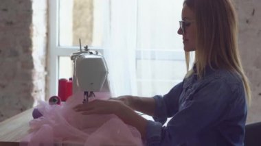 Dikiş atölyesindeki güzel terzi sarışın dikiş makinesiyle çalışıyor. Bir çizgi oluşturur