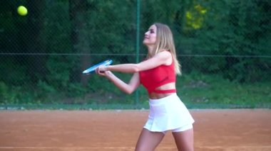 Genç, güzel bir kadın tenis oynar. Kırmızı eşofmanlı bir kız profesyonel olarak tenis antrenmanı yapıyor.