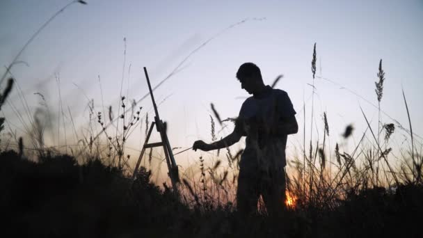 Силуэт мужчины-художника, рисующего пейзаж заката на природе — стоковое видео