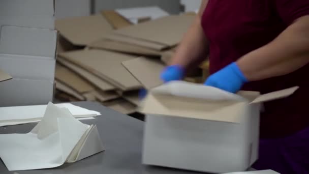 En fabriksarbetare lägger papper i mitten av en tom låda och sätter det på en transportör — Stockvideo