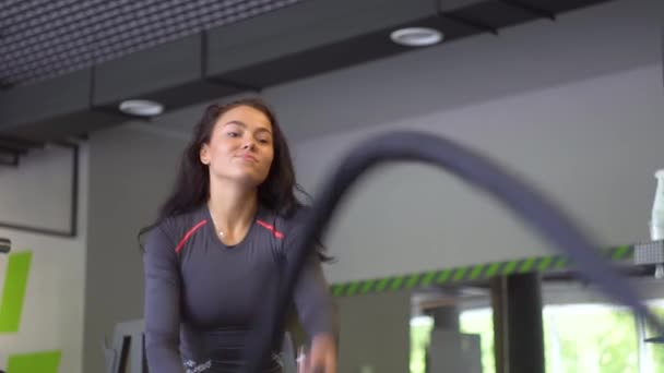 Jovem se exercitando duro com corda de batalha durante a sessão de treinamento cruzado. Menina bonita no clube de esportes faz diferentes tipos de exercícios sobre os simuladores — Vídeo de Stock