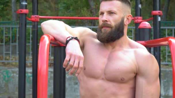 Bodybuilder visar muskler. Ung skäggig atletisk bodybuilder spelar sport utomhus — Stockvideo